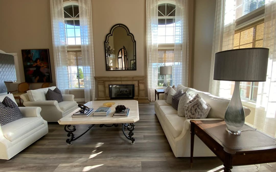 Living room with a cream sofa and matching armchairs reupholstered by Capistrano Upholstery, sheer draperies at tall arched windows