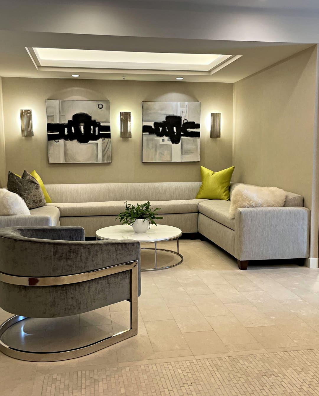 Lounge with a custom sectional, two abstract paintings between sconces and a velvet barrel chair