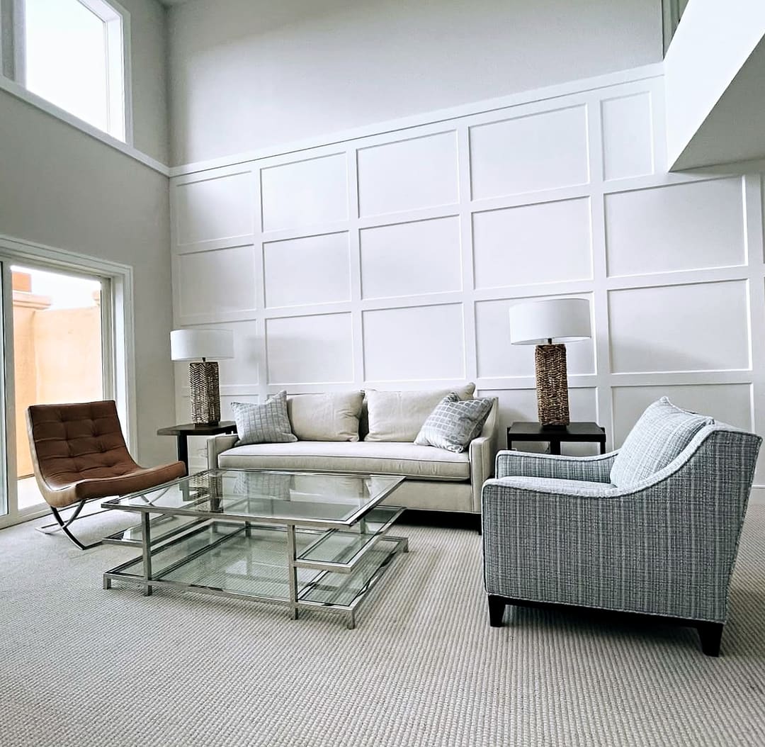 Two-story room with a paneled white wall, a cream sofa, a woven armchair and a tufted leather lounge chair