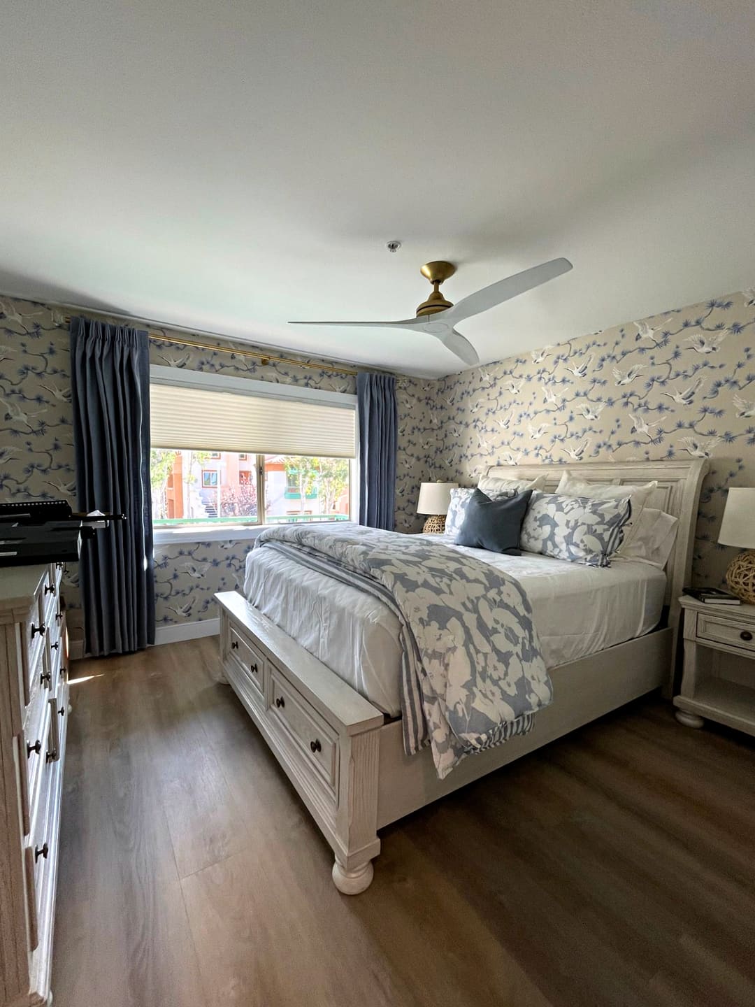 Bedroom with blue linen pleated draperies on a brass rod, crane wallpaper and a white sleigh bed