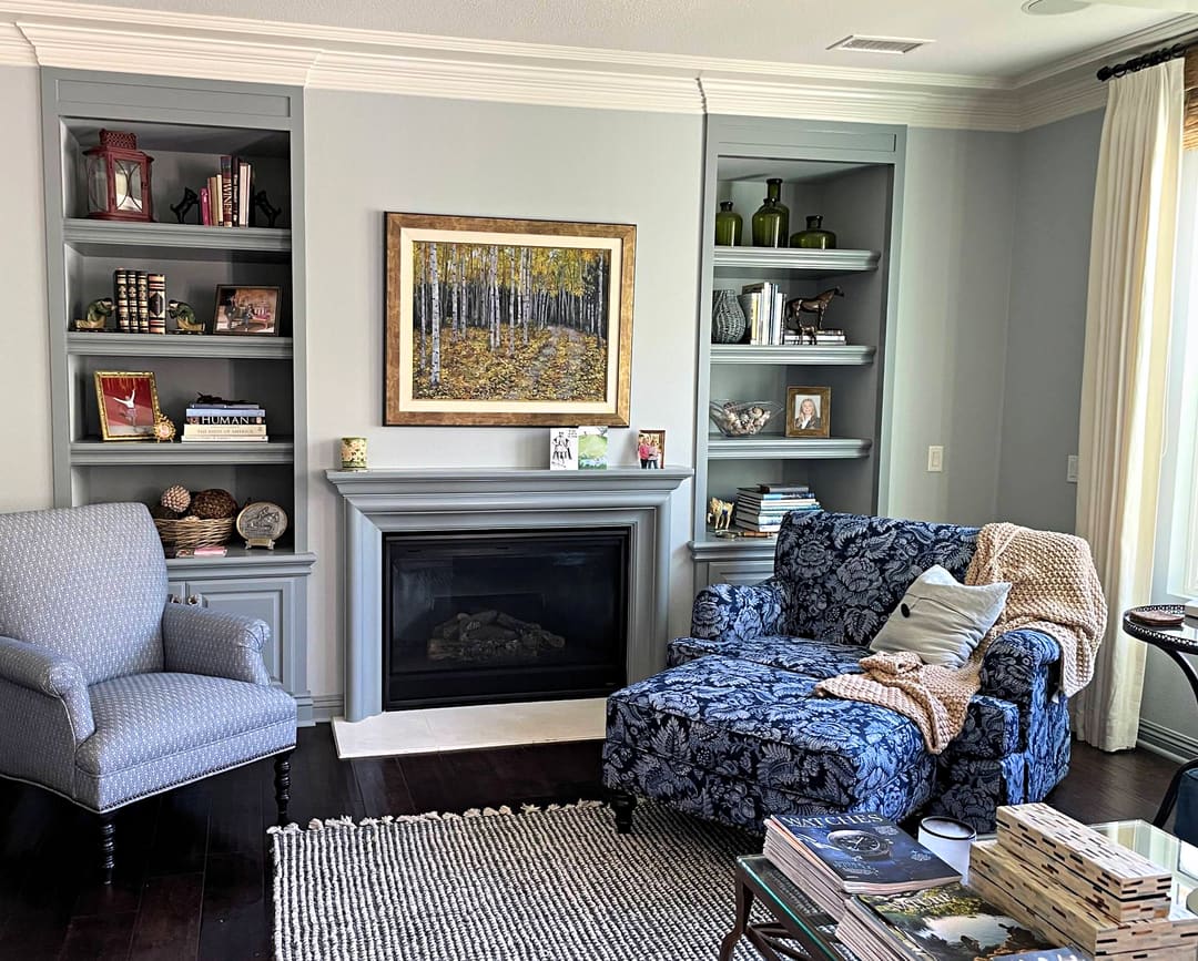 Fireplace with built-in shelves, a blue damask chair and ottoman and a patterned armchair