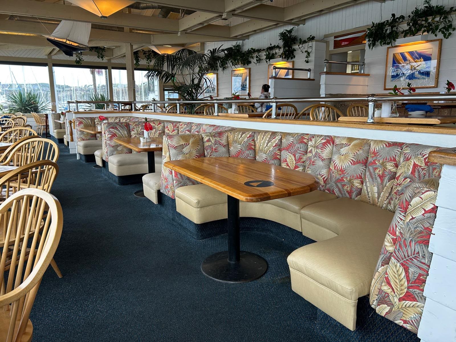 Curved Wind & Sea booths with palm-leaf backs and cream seats, the harbor's masts visible through the windows